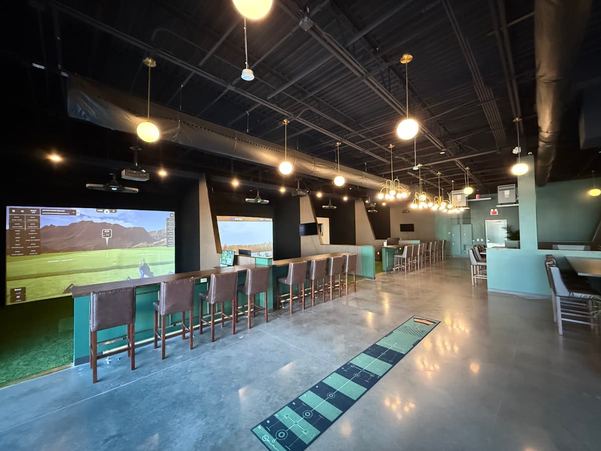 The Clubhouse simulator bays with Foresight Falcon screens, bar seating, and putting practice area